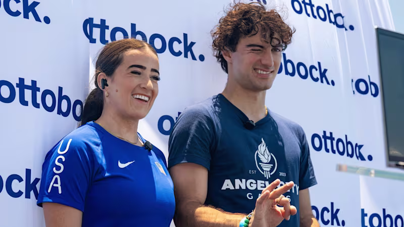 Ezra Frech and Lindi Marcusen smiling in front of an Ottobock banner on stage, ready to give an interview