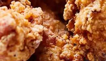 A close-up of a meal at RPM Bar + Grill featuring crispy fried chicken tenders and golden french fries served on a rectangular tray lined with branded paper. In the foreground, two dipping sauces, one yellow and one brown, are placed in small metal ramekins. A drink is blurred in the background.