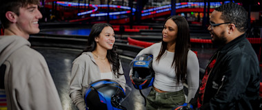 Close-up of a gloved person holding a racing steering wheel, with a digital screen and controls in the background. The steering wheel features the logo "R1". The atmosphere suggests a high-tech racing environment, possibly a simulation or an actual race car.