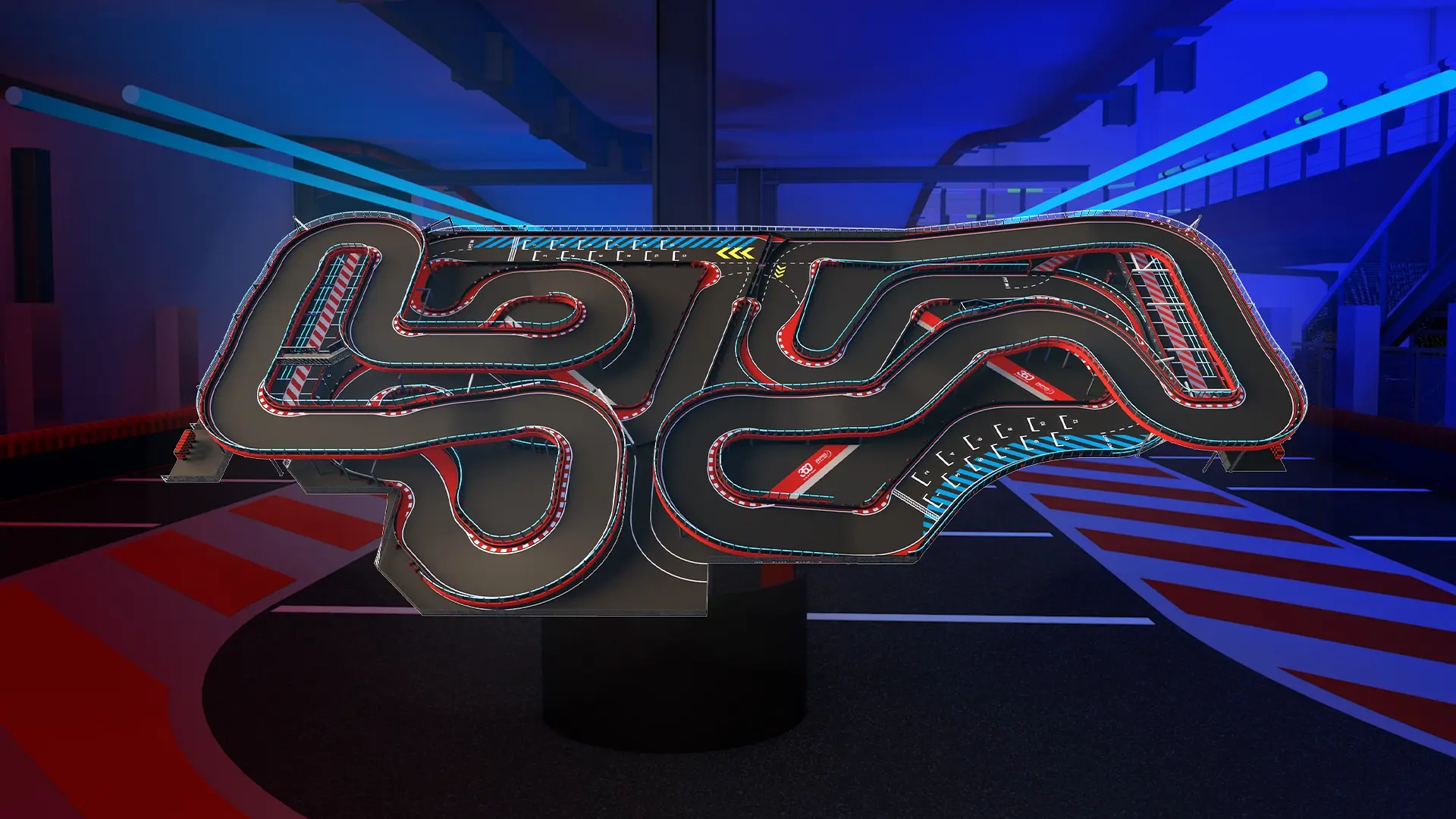 A complex indoor go-kart track with multiple winding turns, lit under blue and red lights. The track layout features several straightaways and sharp corners, designed for a challenging racing experience. The background includes part of the racing facility with additional lighting.