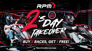 Two people racing go-karts indoors, wearing helmets and race suits, with dramatic lighting and red accents. The text "RPM – Race Play More 2's Day Takeover Buy 2 races, get 1 free! *Terms & Conditions may Apply" is displayed prominently in the image.