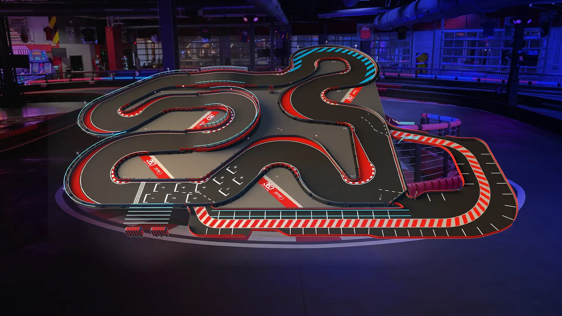 An indoor go-kart track featuring a complex and winding layout with multiple tight turns and straightaways. The track has red, white, and blue markings, with safety barriers along the edges. The surrounding area is dimly lit with a few visible structures.