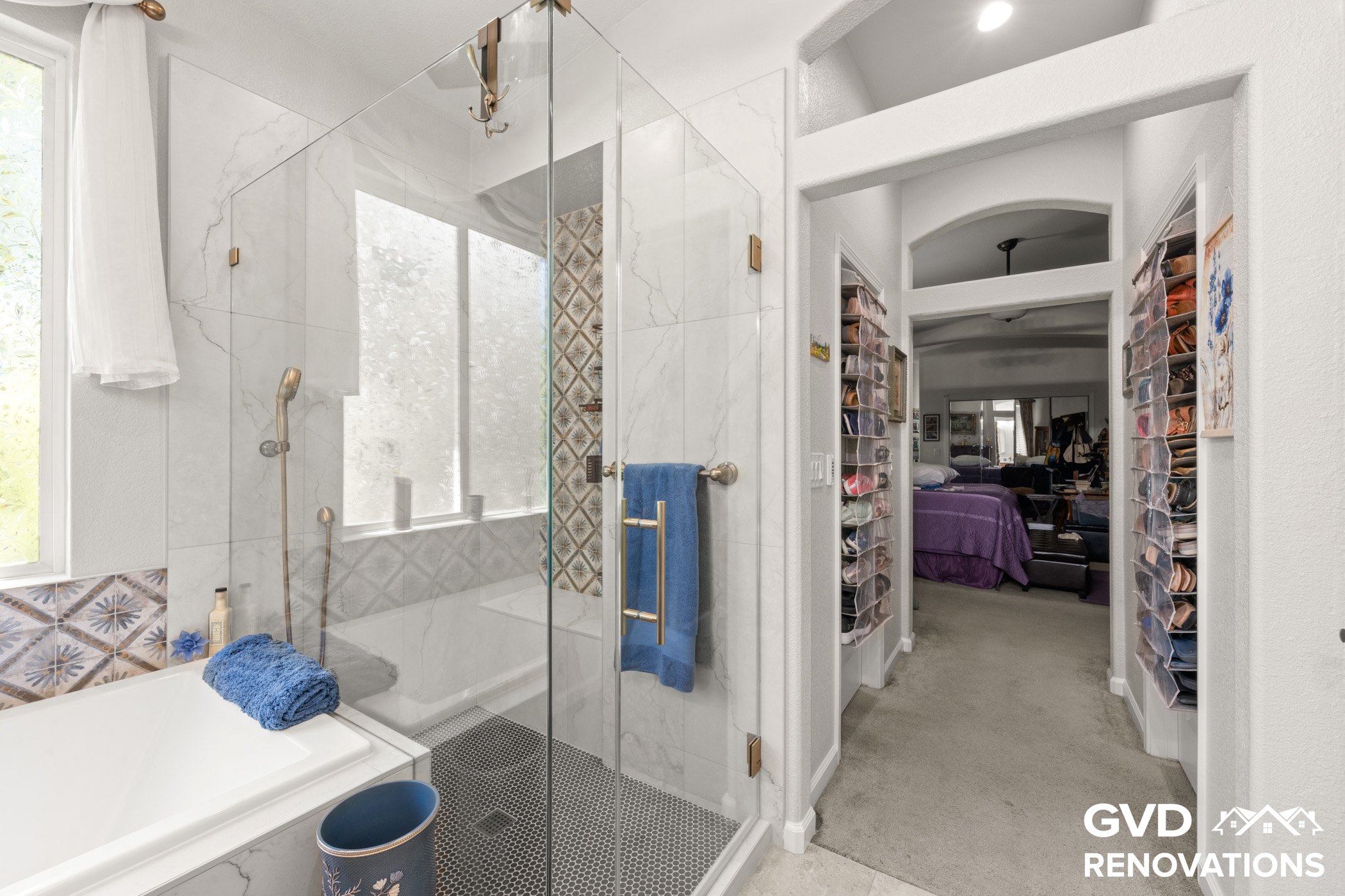 Frameless glass shower with marble tile beside the walk-in closet doorway