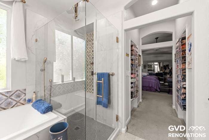 Frameless glass shower with marble tile beside the walk-in closet doorway