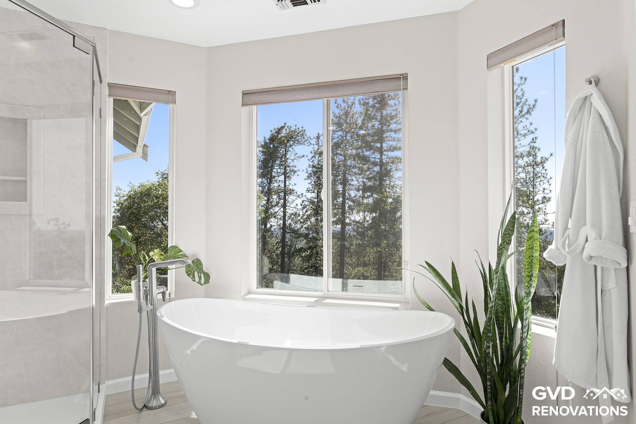 Freestanding soaking tub set beneath large windows with a tub filler