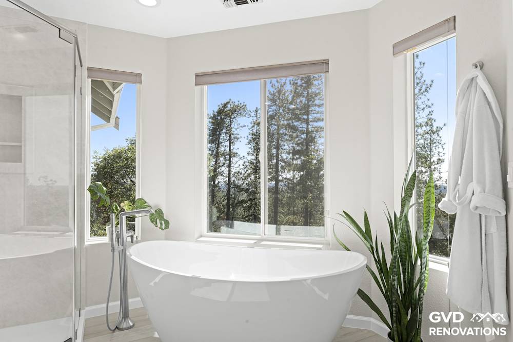 Freestanding soaking tub set beneath large windows with a tub filler