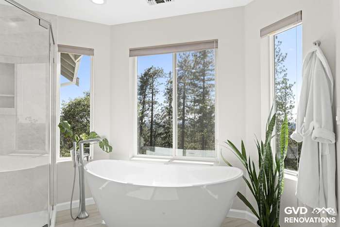 Freestanding soaking tub set beneath large windows with a tub filler