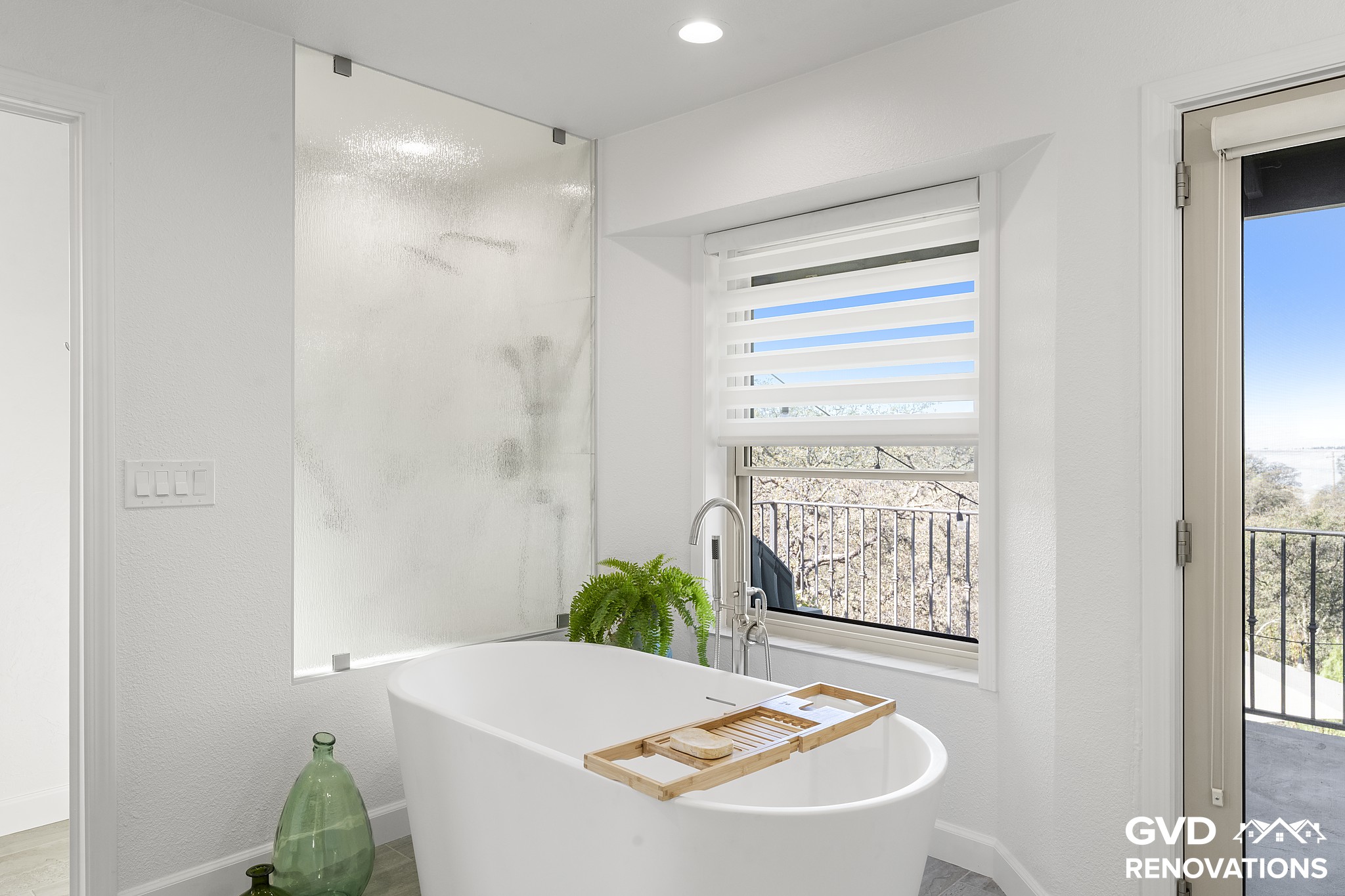 Freestanding soaking tub beside the marble-look walk-in shower with frameless glass