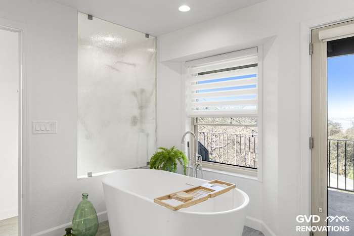Freestanding soaking tub beside the marble-look walk-in shower with frameless glass