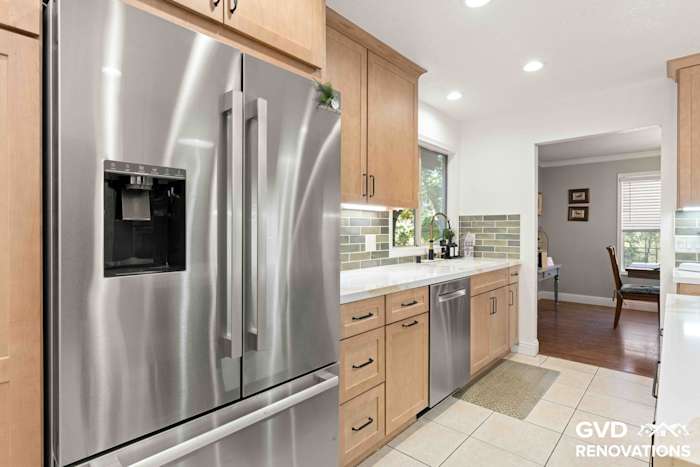 Stainless steel French-door refrigerator and dishwasher alongside maple cabinets in the remodeled kitchen