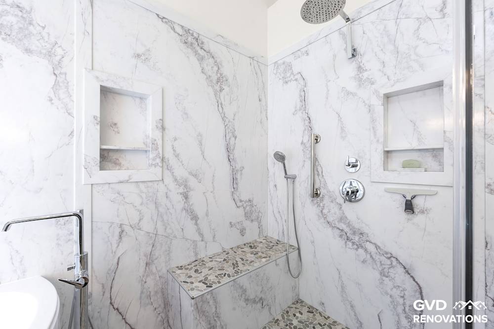 Marble-look walk-in shower with a rainfall head, recessed niche, tiled bench and grab bar