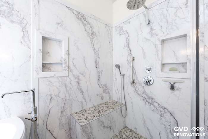 Marble-look walk-in shower with a rainfall head, recessed niche, tiled bench and grab bar