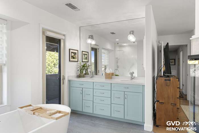 Sage-green double vanity with a makeup station and framed mirror in the remodeled primary bath