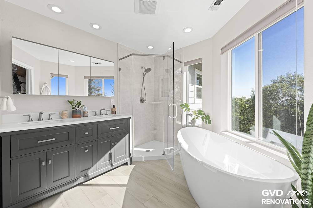 Remodeled primary bathroom in Greenwood with a charcoal double vanity, a freestanding soaking tub and a neo-angle walk-in shower