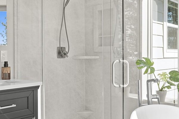 Remodeled primary bathroom in Greenwood with a charcoal double vanity, a freestanding soaking tub and a neo-angle walk-in shower
