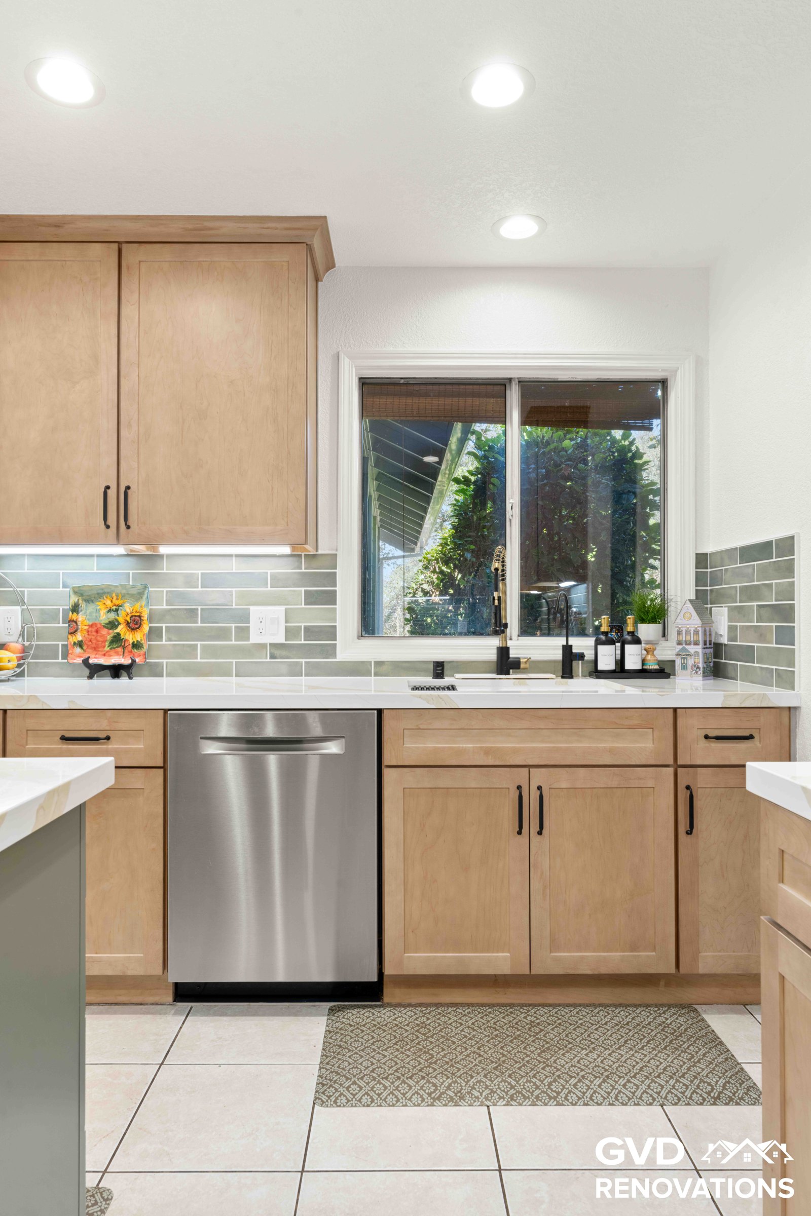 Kitchen sink and stainless steel dishwasher below a garden window with quartz counters