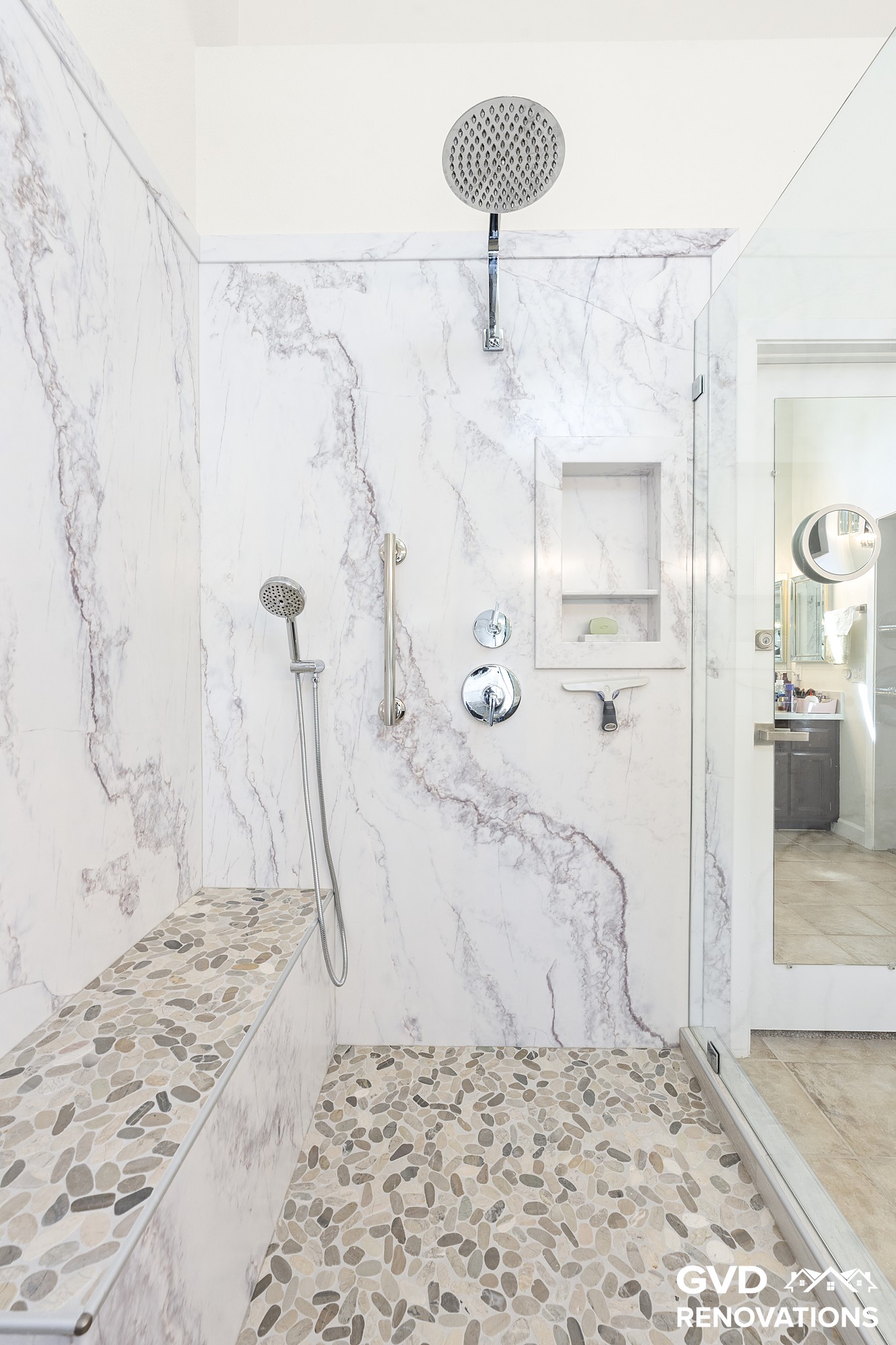 Walk-in shower in marble-look tile with a rainfall head above a pebble mosaic floor