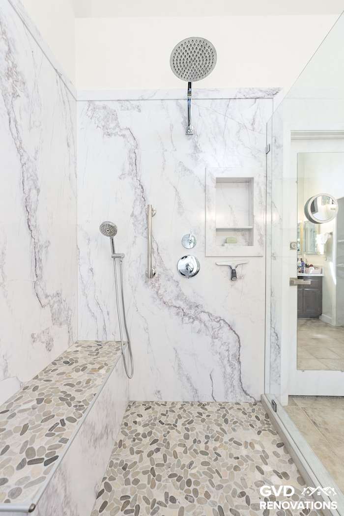 Walk-in shower in marble-look tile with a rainfall head above a pebble mosaic floor
