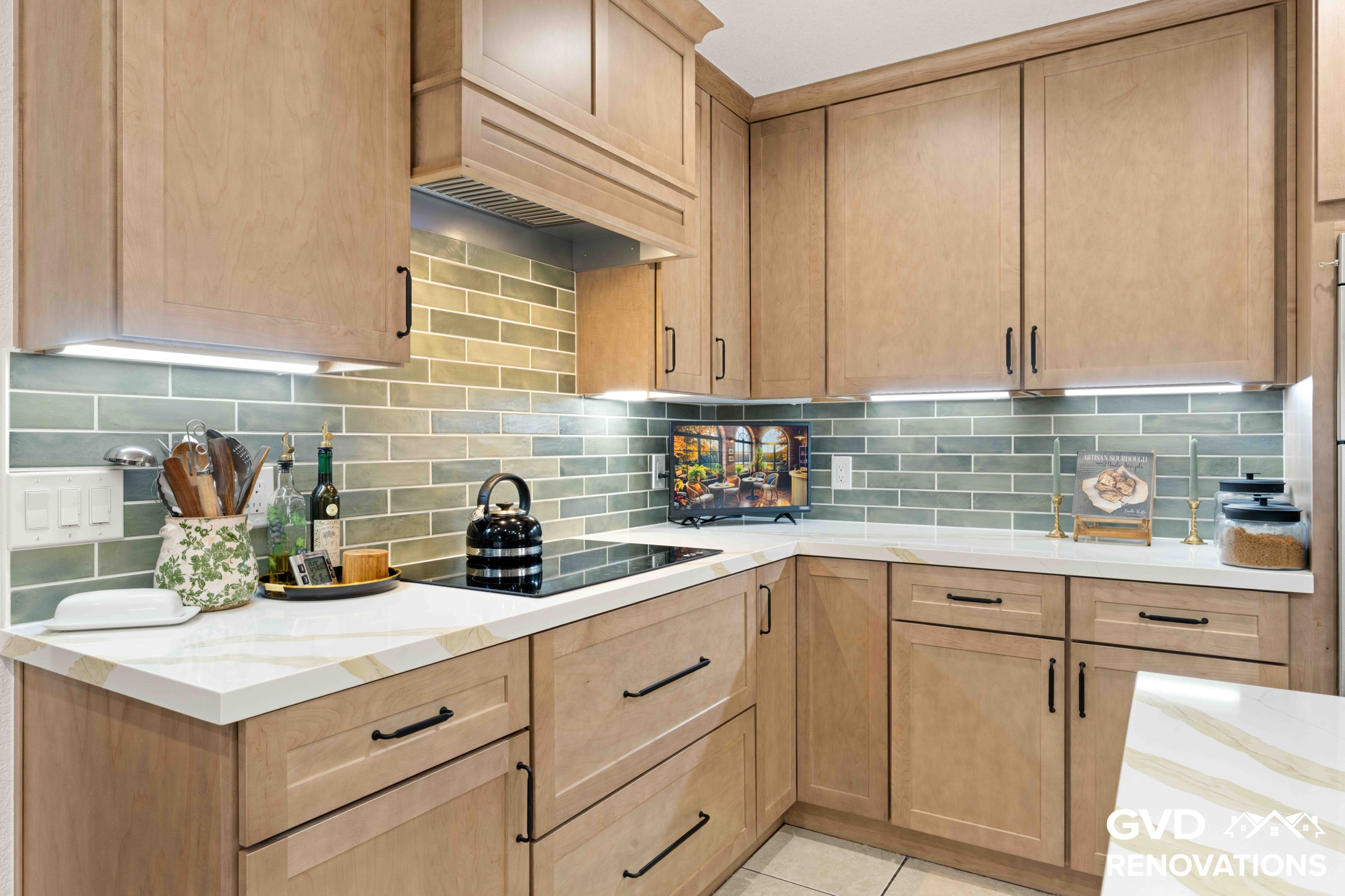L-shaped maple kitchen with an electric cooktop, quartz counters, sage green subway tile backsplash and under-cabinet lighting