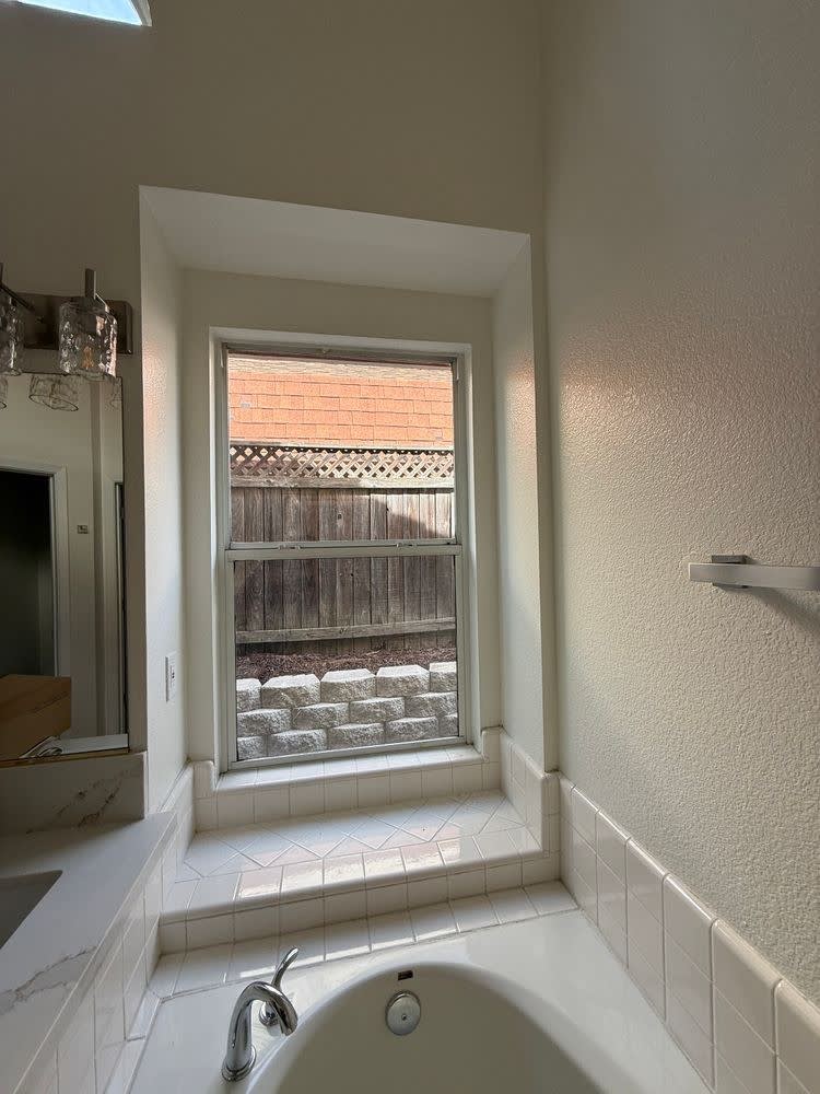 Before: original drop-in oval soaking tub set beneath the window with a white tile surround