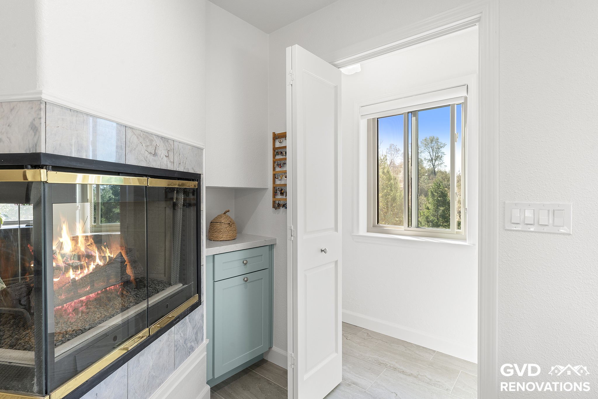 Three-sided gas fireplace with a marble-look tile surround beside a new window