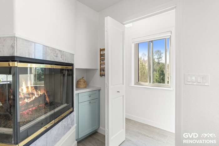 Three-sided gas fireplace with a marble-look tile surround beside a new window