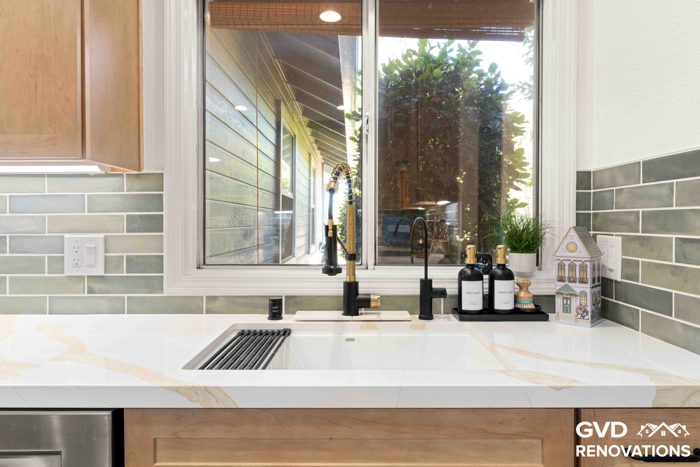 Undermount stainless steel sink with a black spring-neck faucet set below a backyard window with Calacatta quartz counters
