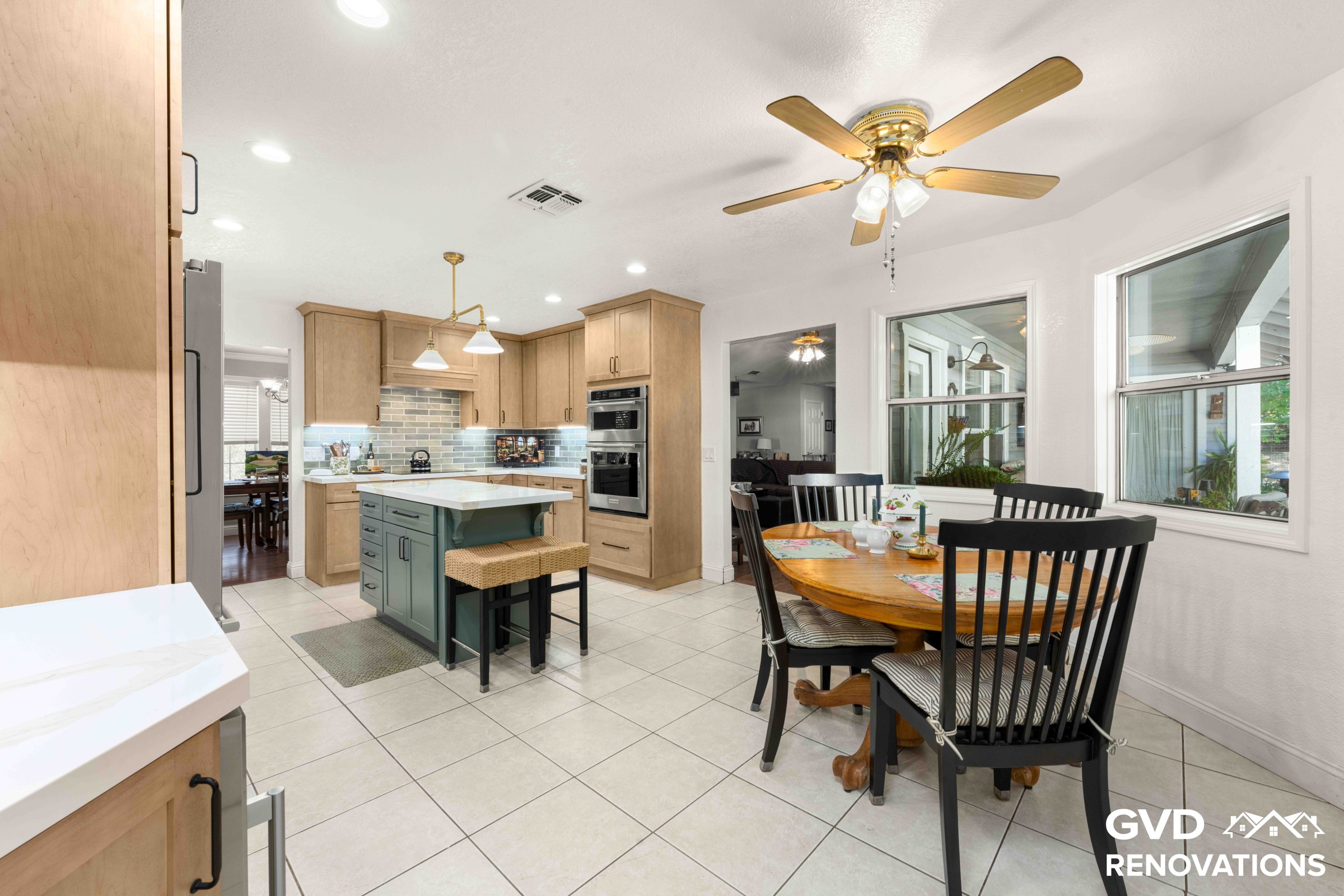 Wide view of the remodeled kitchen from the dining area with maple cabinets, a sage green island and stainless appliances