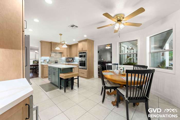 Wide view of the remodeled kitchen from the dining area with maple cabinets, a sage green island and stainless appliances