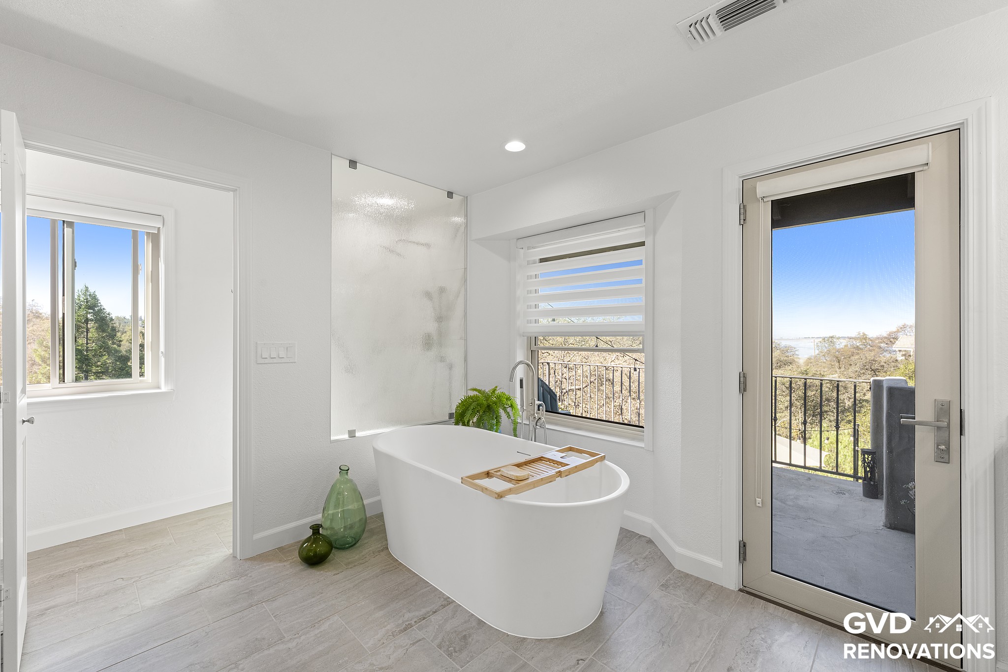 Freestanding soaking tub beneath new windows with a glass door to the deck