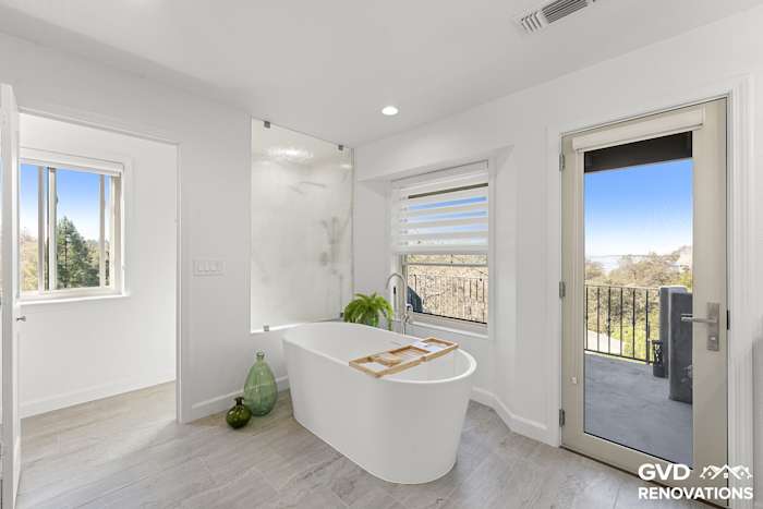 Freestanding soaking tub beneath new windows with a glass door to the deck