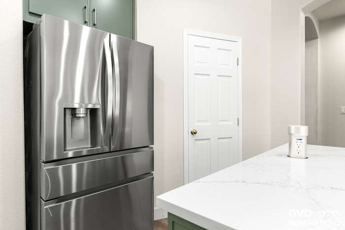 Stainless French-door refrigerator beside a built-in pantry in a sage green kitchen