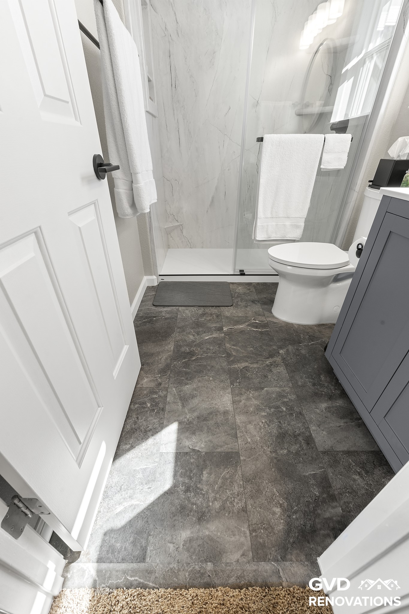 Grey vanity and toilet with dark-tone flooring in the remodeled hall bath