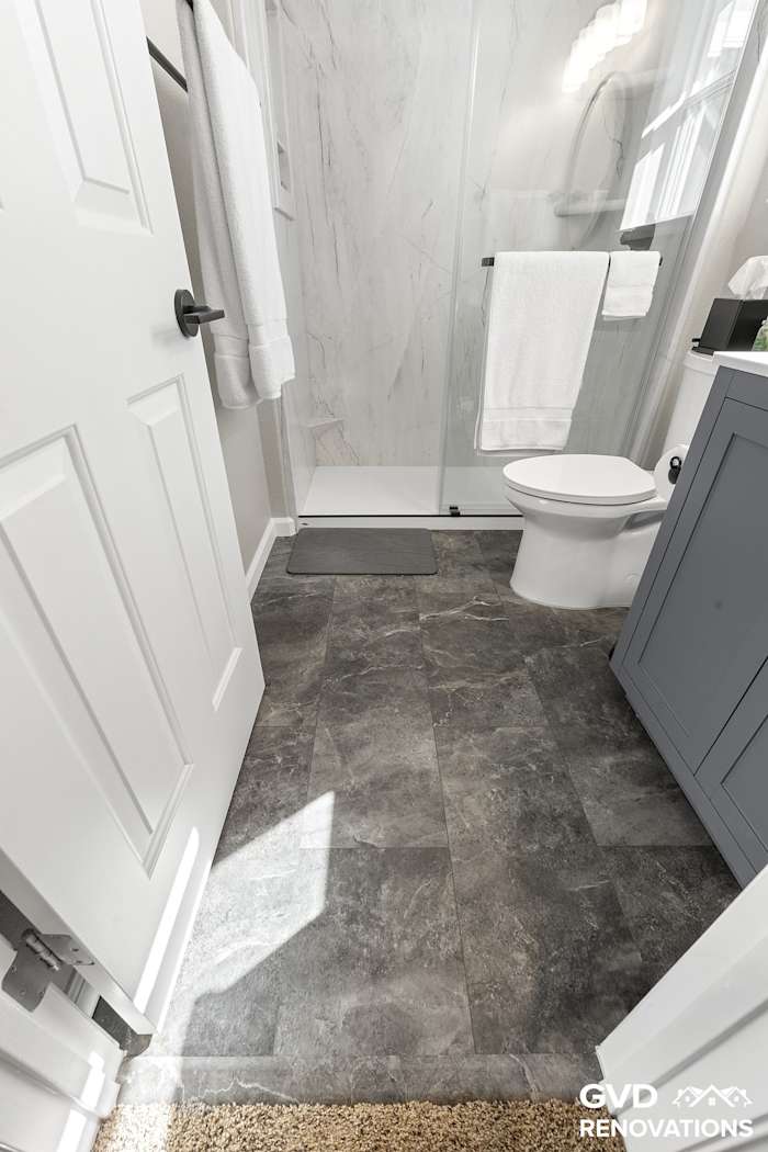 Grey vanity and toilet with dark-tone flooring in the remodeled hall bath