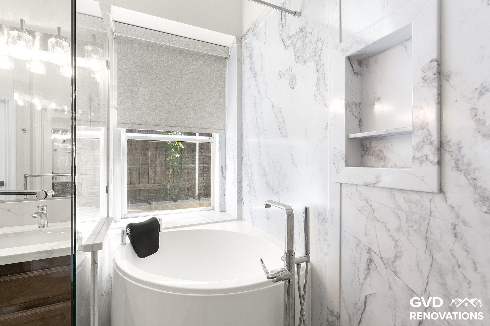 Freestanding soaking tub beneath a window framed by large-format marble-look tile