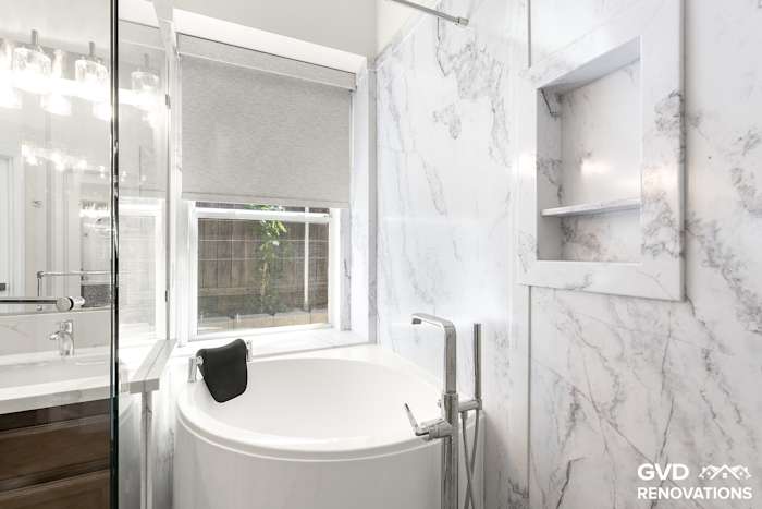 Freestanding soaking tub beneath a window framed by large-format marble-look tile