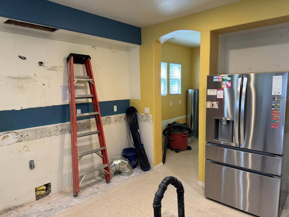 Before: original kitchen during demolition with the cabinetry removed, yellow walls and dated vinyl flooring