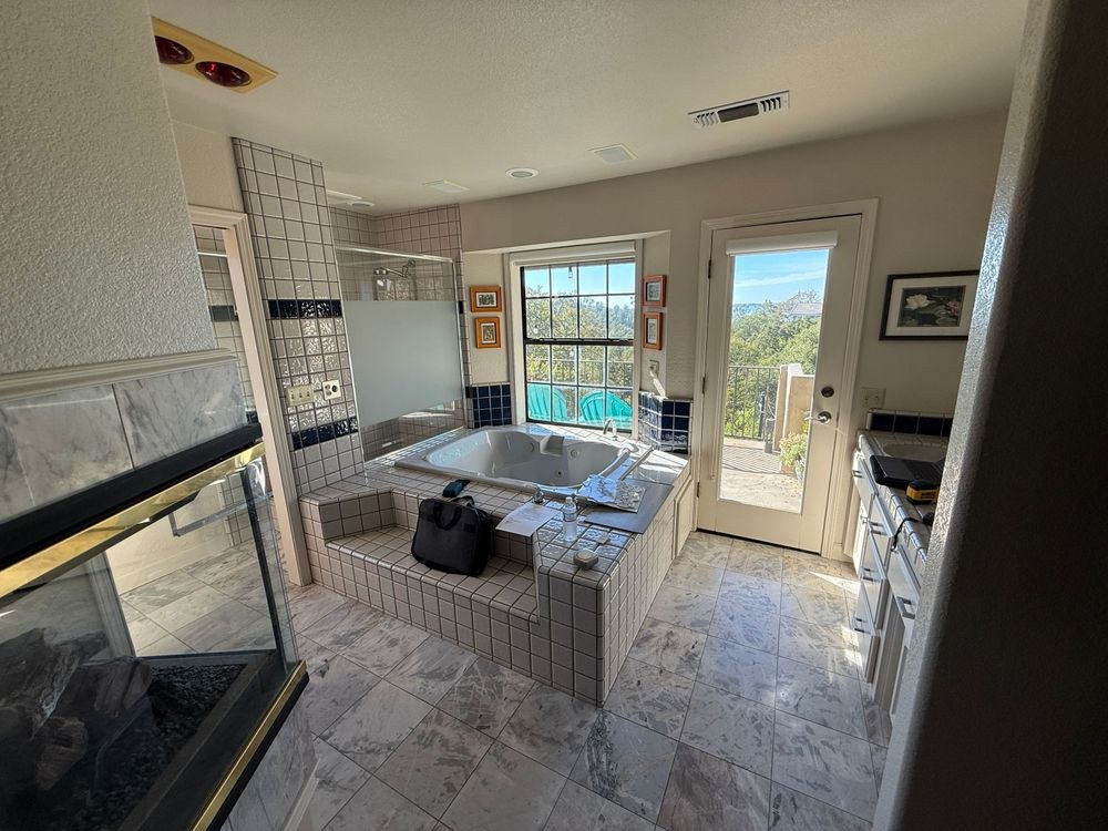 Before: original master bathroom with a drop-in jetted tub on a tile platform, a three-sided fireplace and a marble-tile floor
