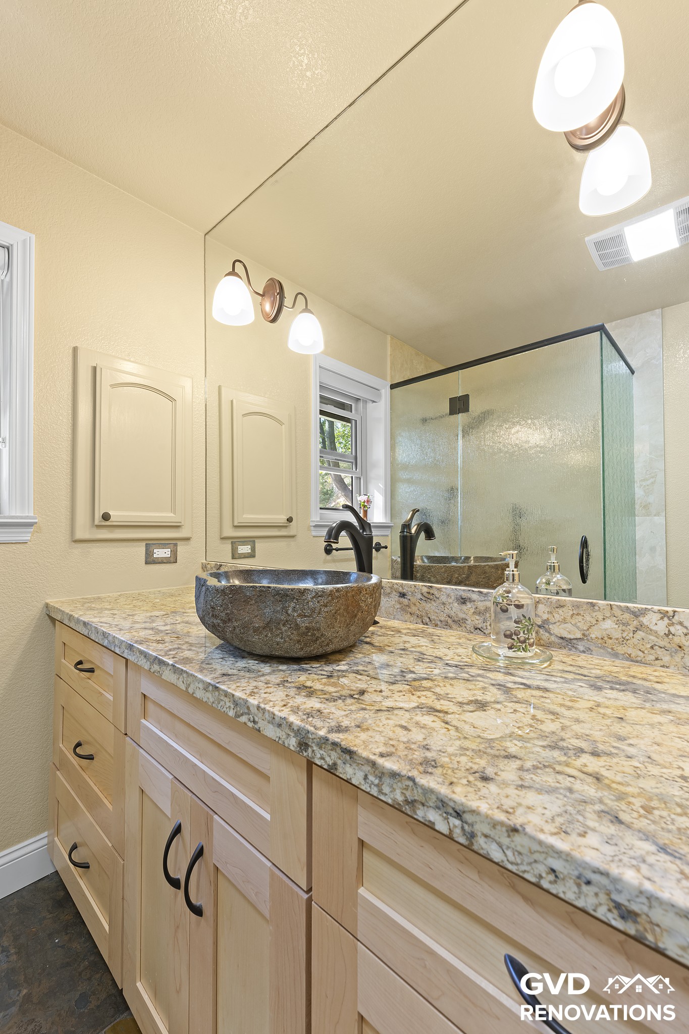 Maple vanity with a stone vessel sink and granite countertop in the remodeled guest bath