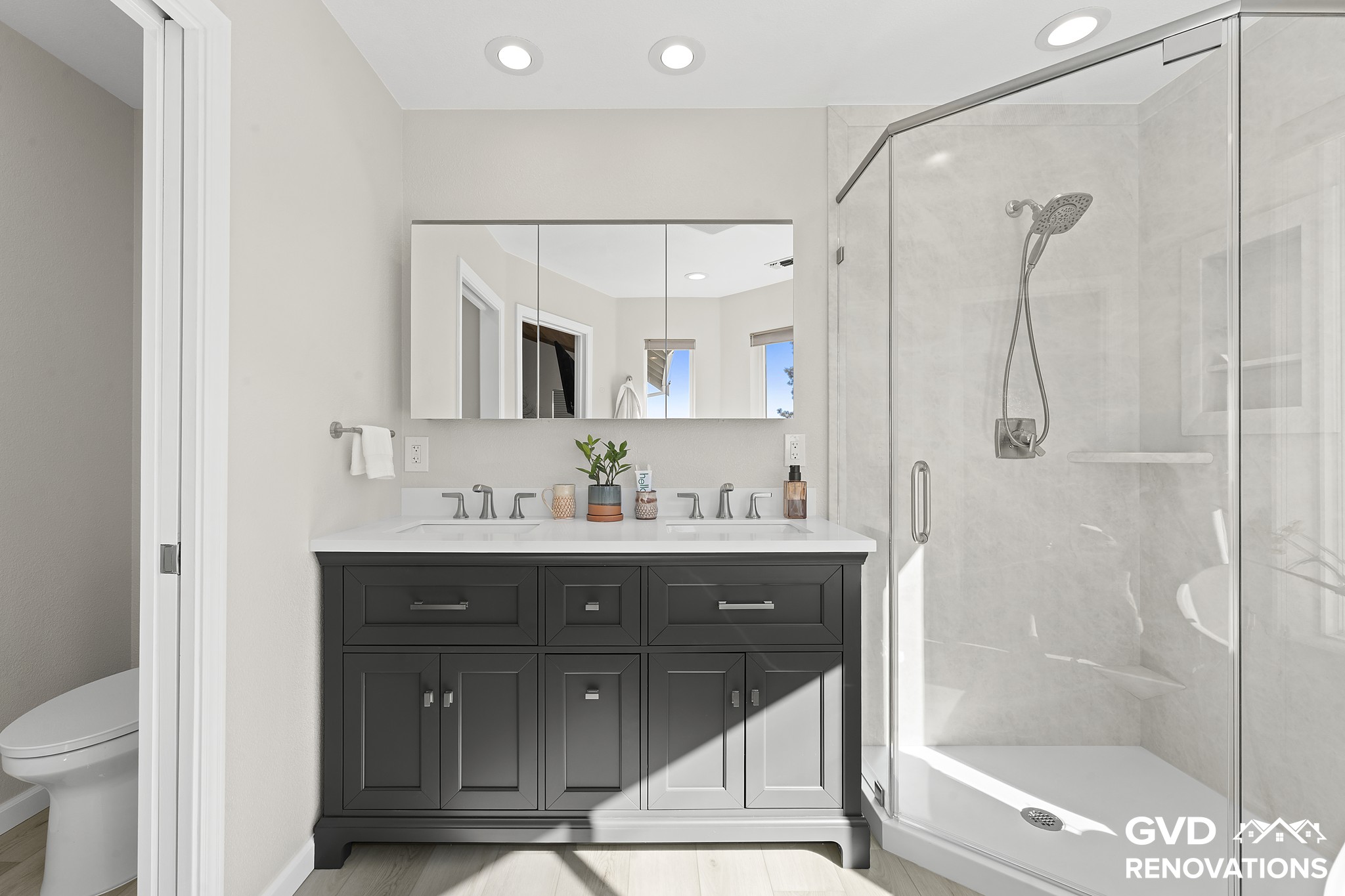 Charcoal double vanity with a framed mirror beside a marble-look neo-angle walk-in shower