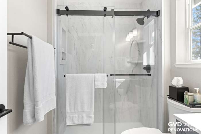 Semi-frameless sliding glass shower door over marble-look solid-surface walls