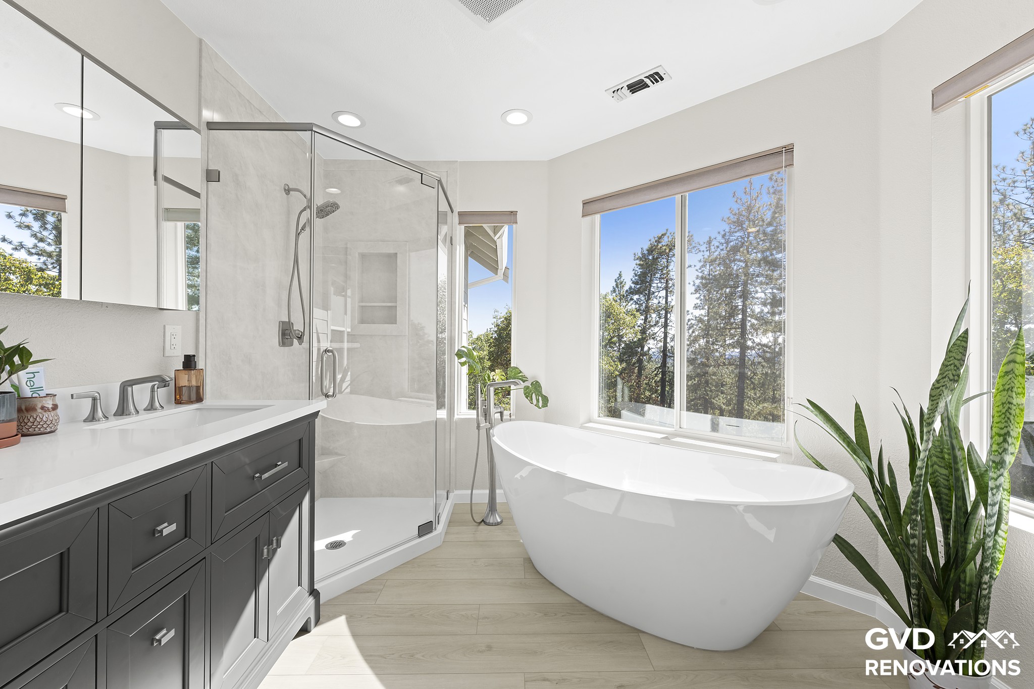 Primary bath with a charcoal double vanity, freestanding tub and a marble-look neo-angle shower by the windows
