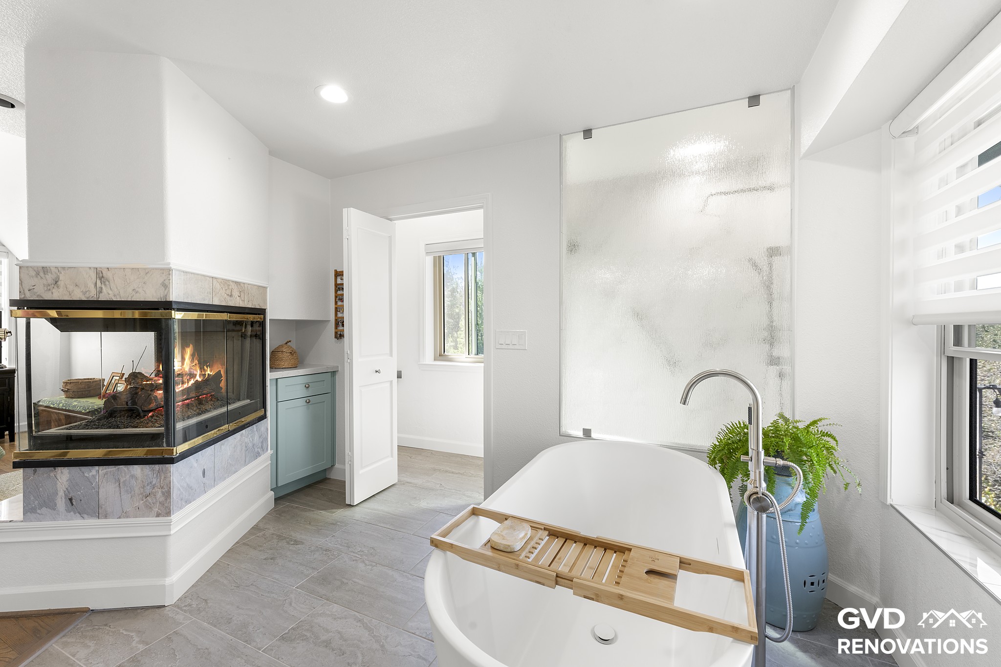 Freestanding soaking tub beside a three-sided fireplace with a marble-look surround