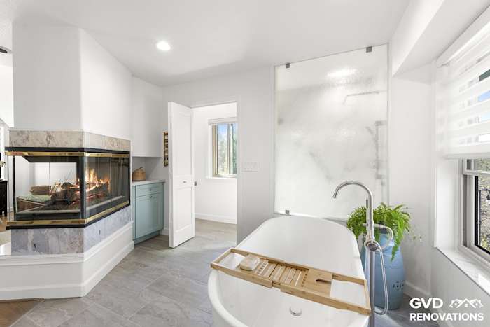 Freestanding soaking tub beside a three-sided fireplace with a marble-look surround
