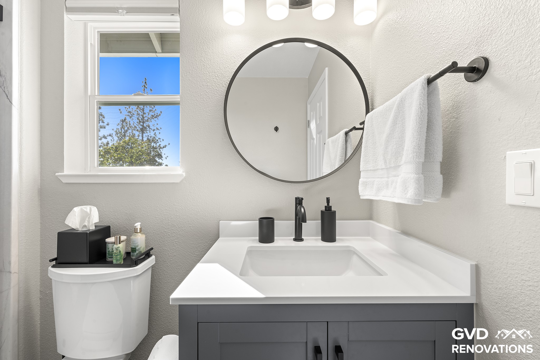 Grey vanity with matte-black fixtures and a round mirror beside a window