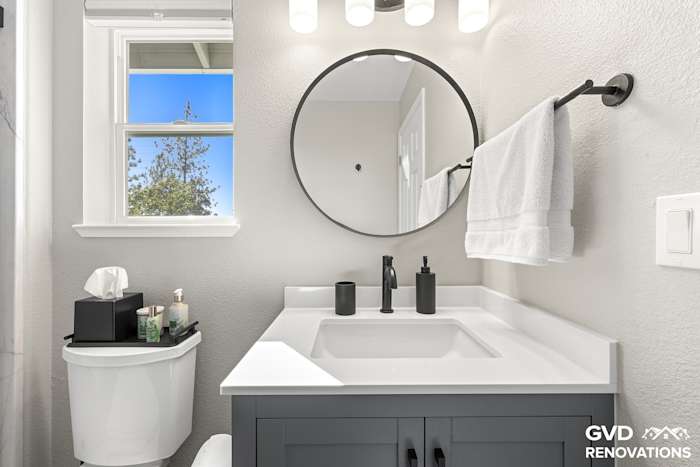 Grey vanity with matte-black fixtures and a round mirror beside a window