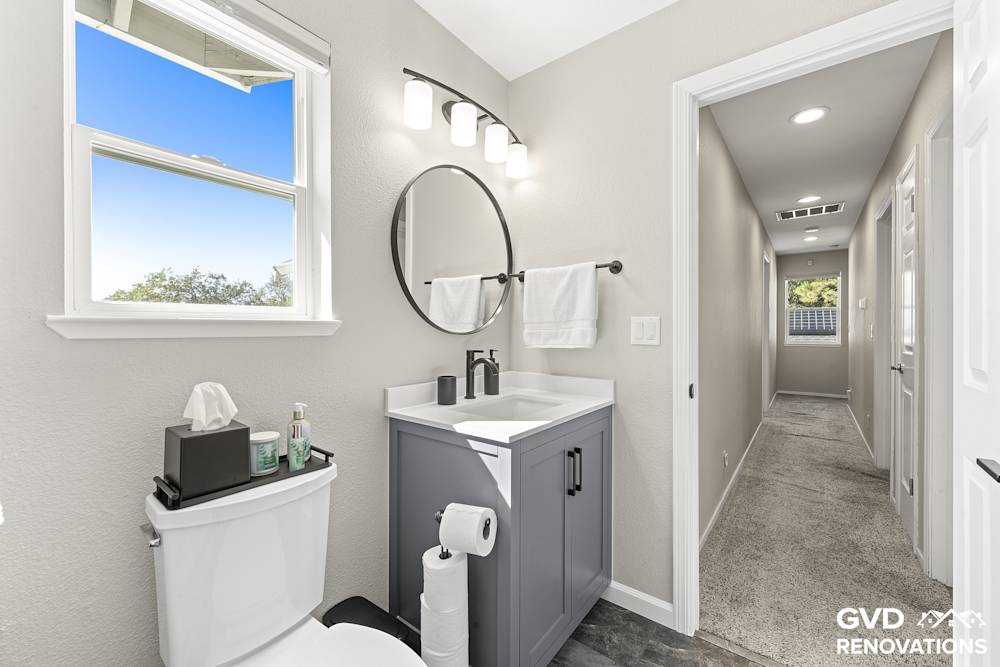 Grey vanity with a quartz countertop and a round black-framed mirror below a window