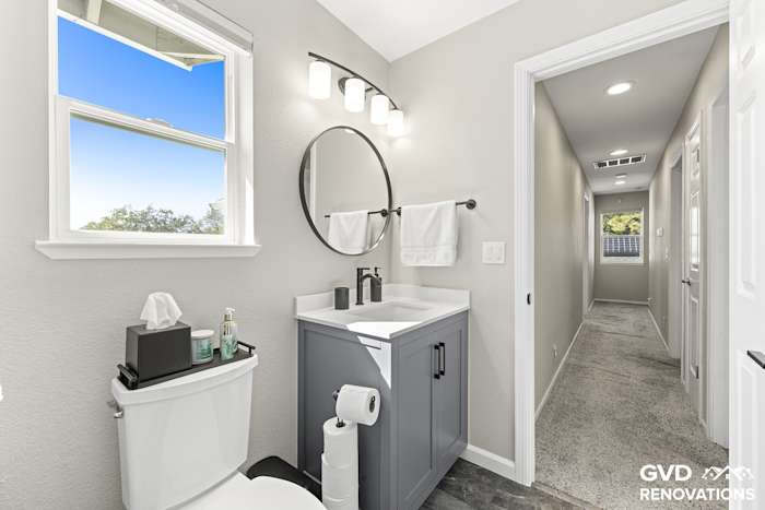 Grey vanity with a quartz countertop and a round black-framed mirror below a window