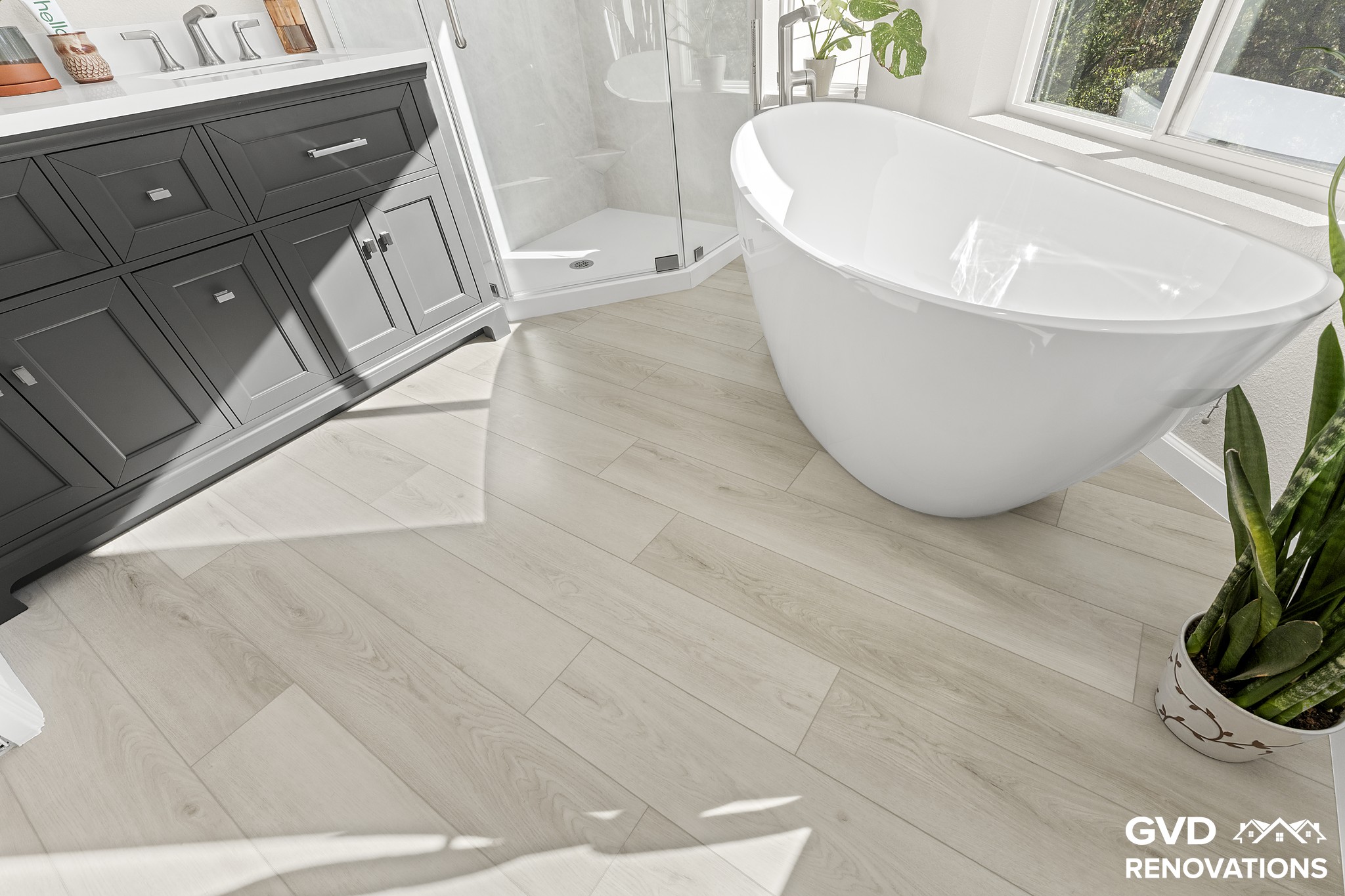 Charcoal double vanity beside a freestanding soaking tub with wood-look flooring