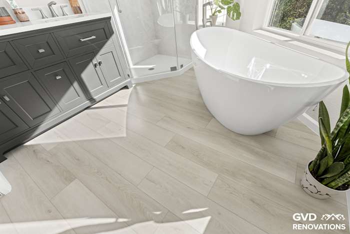Charcoal double vanity beside a freestanding soaking tub with wood-look flooring